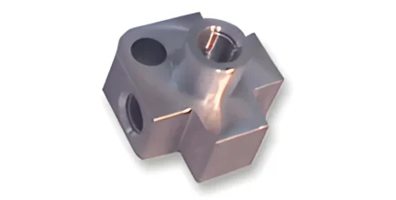 A metallic, cross-shaped component with a smooth surface and multiple holes visible on different sides. The part features one larger cylindrical hole at the top center and two smaller holes on either side, with a light reflection indicating a shiny finish
