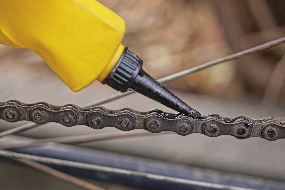 A nozzle, secured to a bottle, is touching a bike chain.