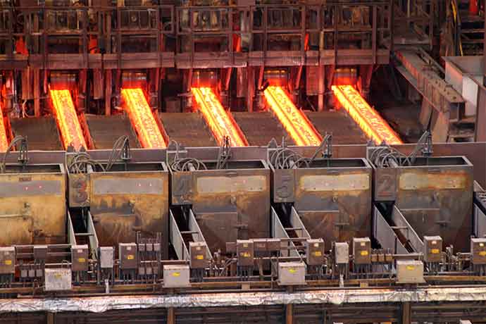 Glowing hot steel slabs on rollers inside an industrial steel mill, showcasing metal production process.