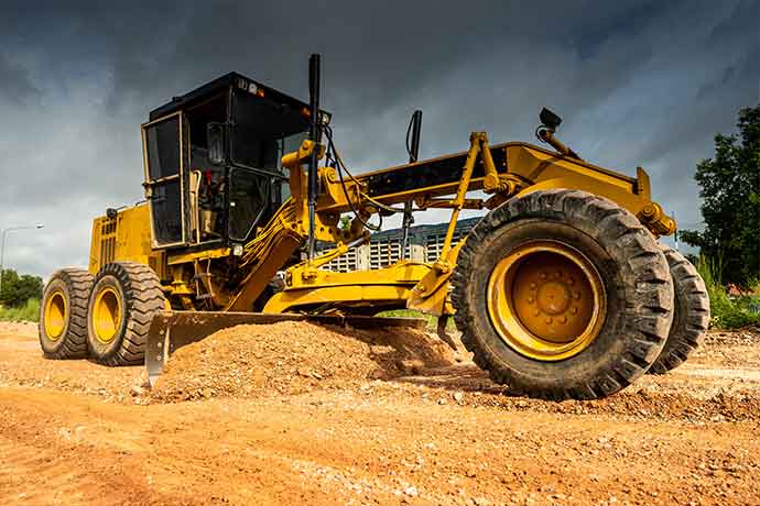Yellow bulldozer leveling dirt on a construction site under a cloudy sky
