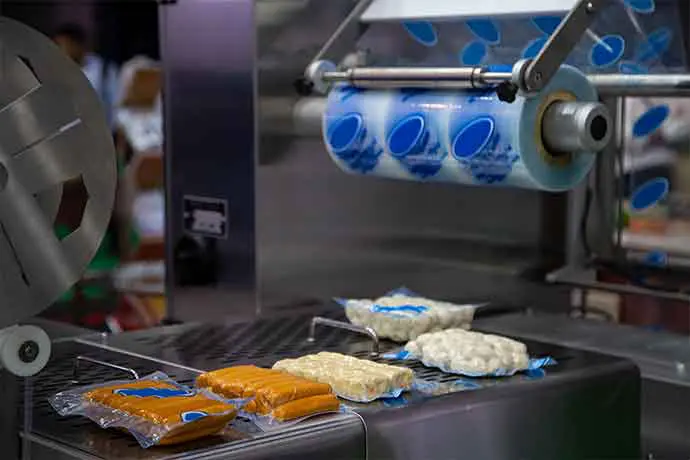 Industrial food packaging machine sealing sausage and cheese products in plastic film.