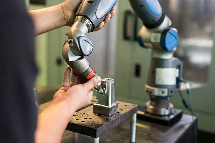 Close-up of hands using a coordinate measuring machine in a manufacturing setting with robotic arms.