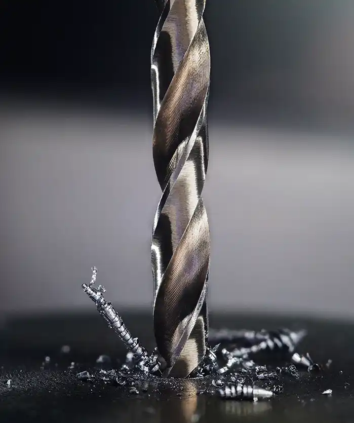 Close-up of a metallic drill bit piercing a surface, with metal shavings scattered below, showcasing precision in machining.