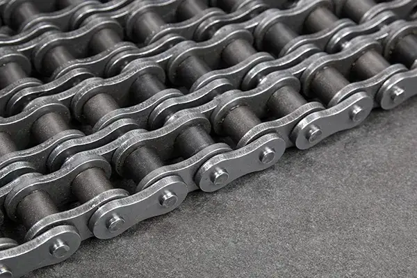 Close-up image of a metal roller chain, showing interlocking links with cylindrical rollers. The chain is arranged in parallel rows on a dark surface, emphasizing its industrial design and metallic texture.
